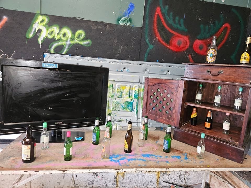 Halloween display with neon Rage and Devil horns signs, TV monitor, decorated wooden cabinet, and beer bottles arranged on a table